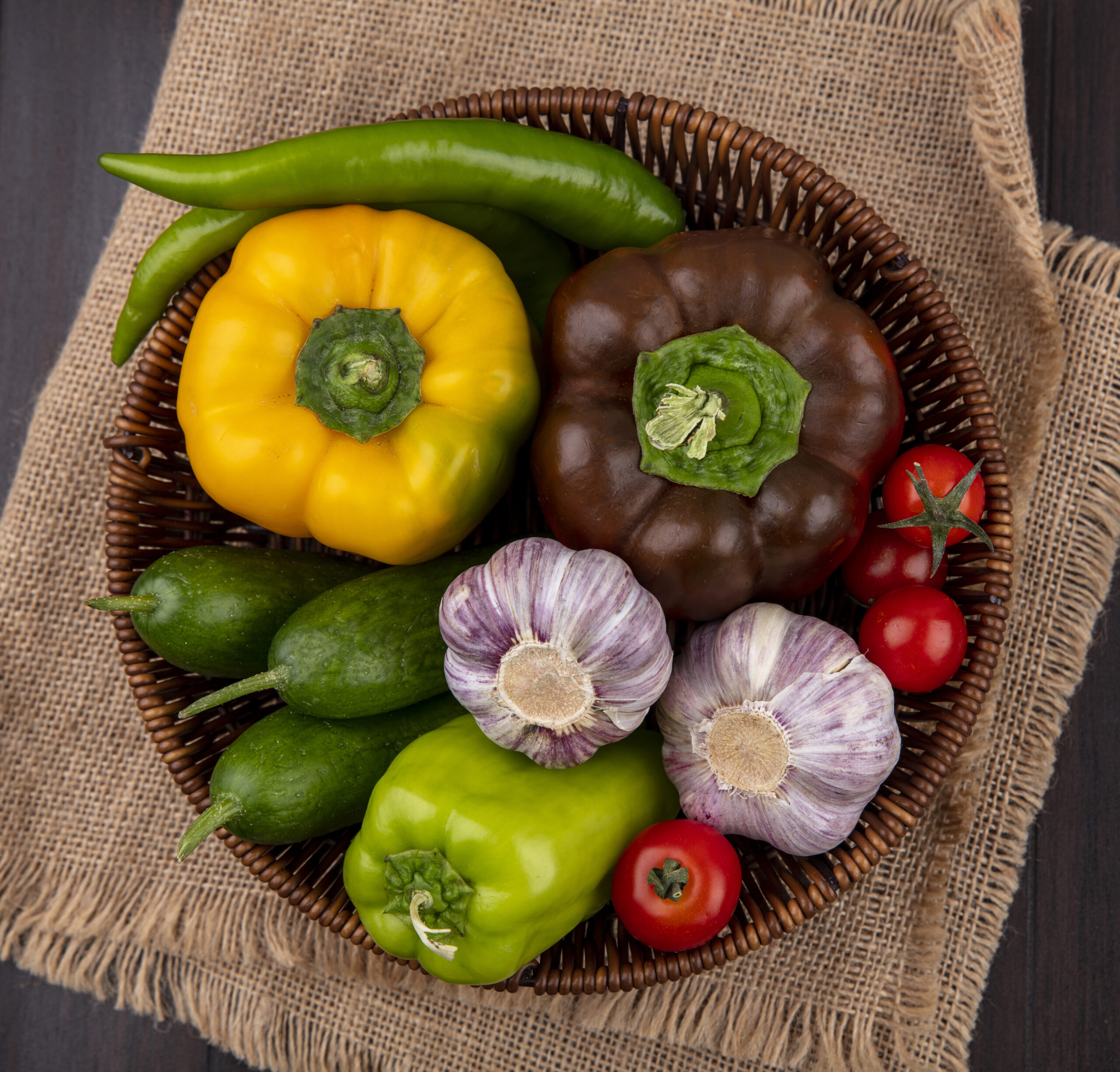 top view of vegetables as pepper tomato cucumber garlic in basket on sackcloth and wooden background
